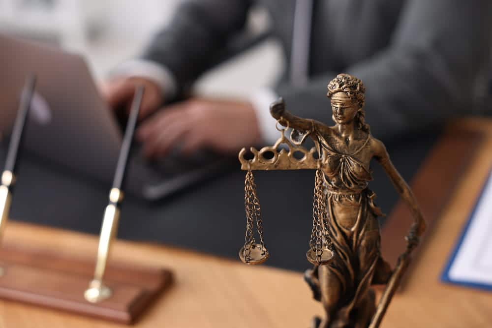 Image is of a Lady Justice statue with an attorney working on a laptop in the background, concept of an alimony attorney preparing legal strategies for spousal support matters.