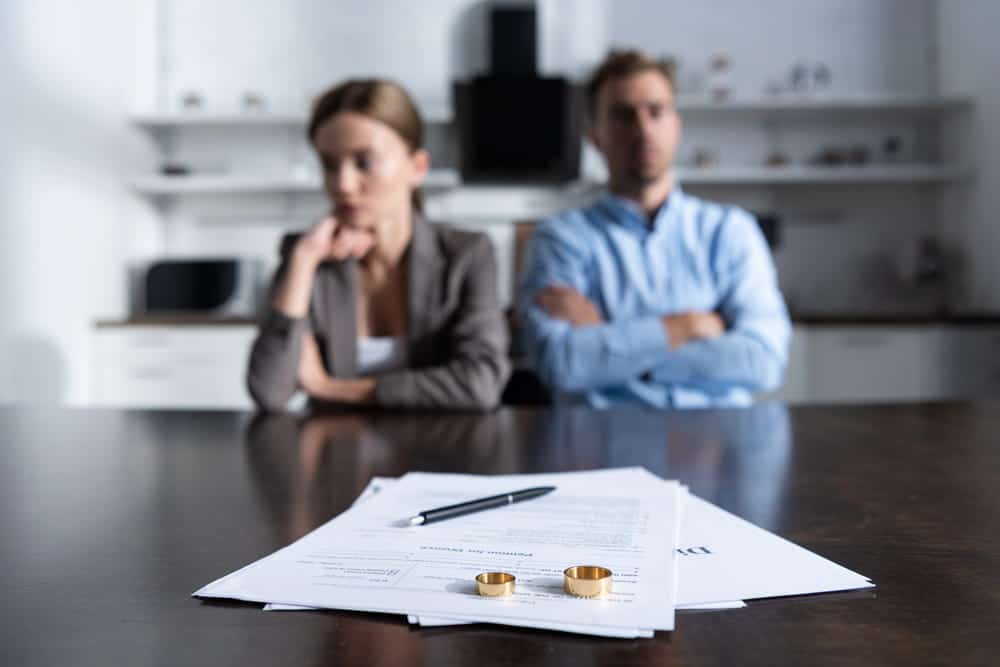 Image is of a couple sitting apart with annulment paperwork and wedding rings on a table, concept of an annulment attorney helping clients determine whether a marriage qualifies for annulment.