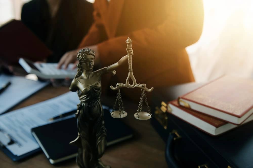 Image is of the Lady Justice statue with legal documents on a desk, concept of a child custody attorney providing family law guidance.