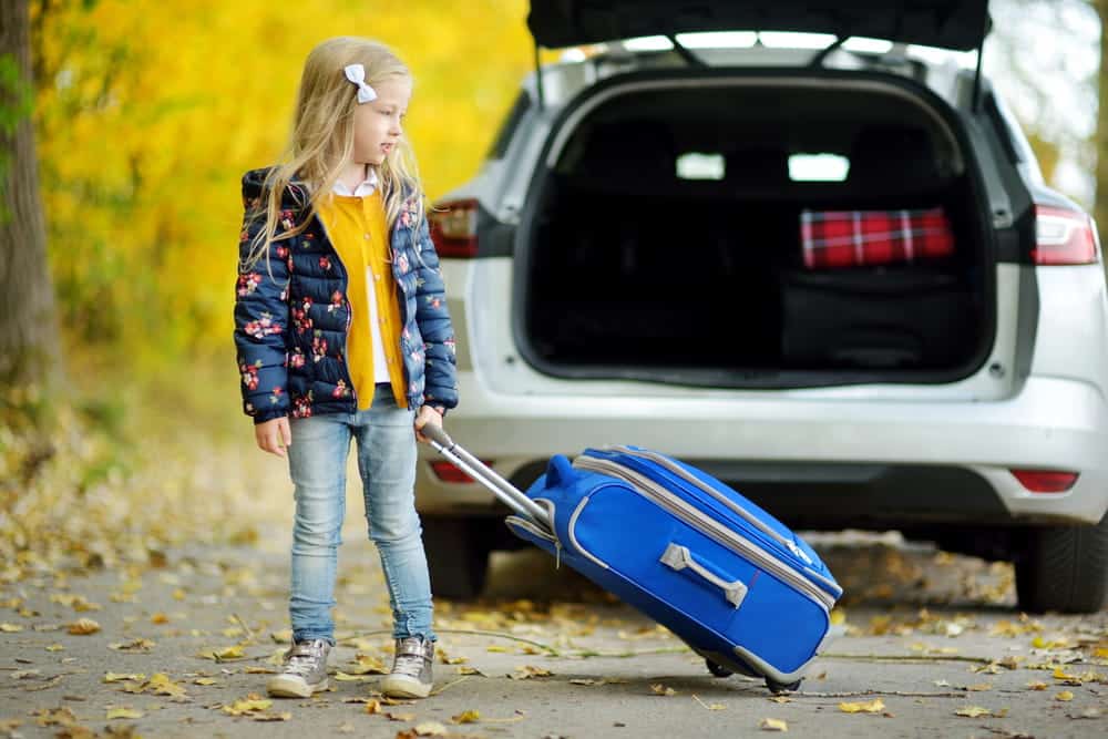Image is of a child standing beside a vehicle with a suitcase before a move, concept of a child relocation & interstate custody attorney.