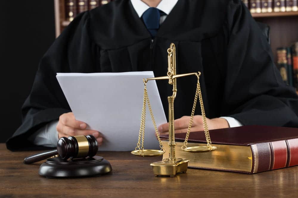 Image is of a judge reviewing legal documents with a gavel and scales of justice, concept of child support modification handled through court proceedings.