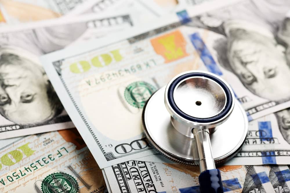 Image is of a stethoscope placed on one hundred dollar bills, concept of child support modification involving healthcare expenses and financial responsibilities.