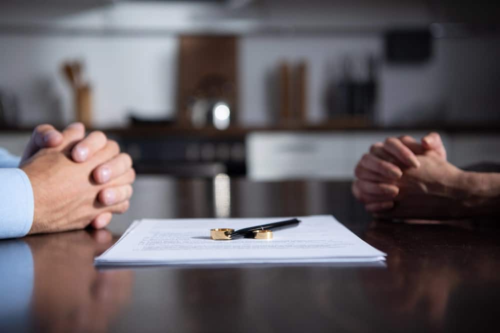 Image is of two spouses seated across from one another with legal documents and wedding rings between them, concept of a collaborative divorce attorney helping couples negotiate a mutually acceptable agreement.