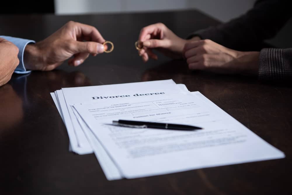 Image is of spouses holding wedding rings above a divorce agreement, concept of a collaborative divorce attorney assisting with negotiated settlement terms.