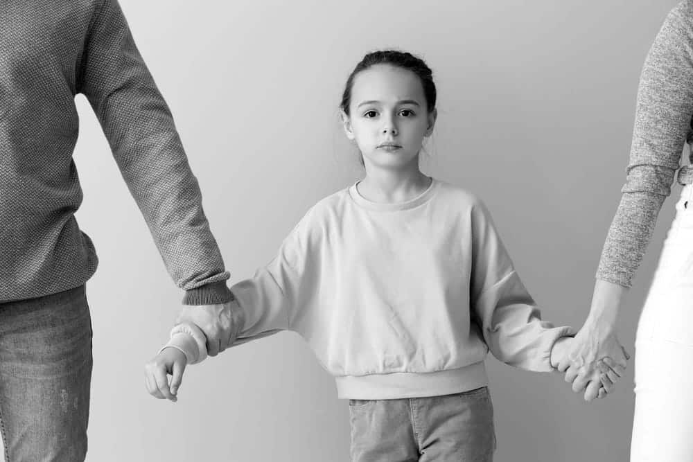 Image is of a child holding both parents' hands during a family dispute, concept of contested divorce attorney