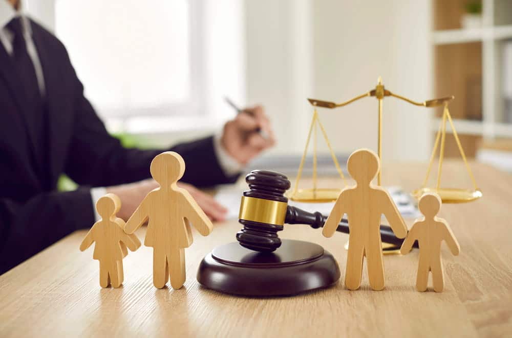 Image is of wooden family figures with a judge's gavel and scales of justice on a desk, concept of divorce attorney