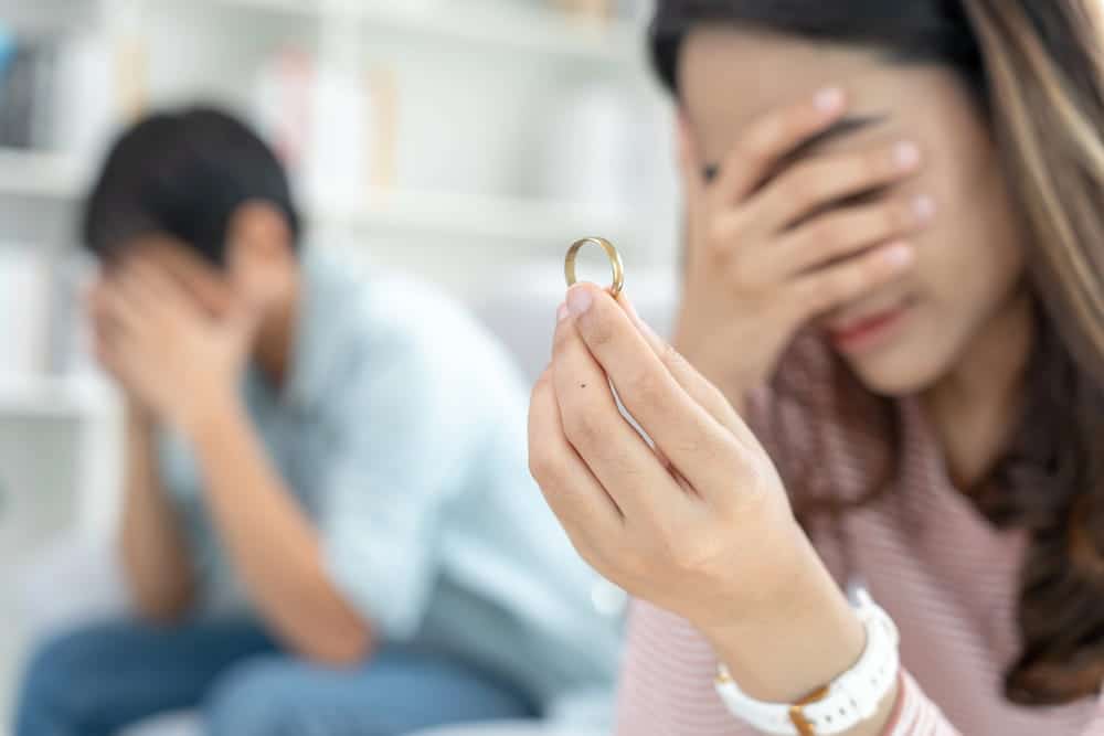 Image is of a woman holding a wedding ring while sitting apart from her spouse, concept of divorce attorney