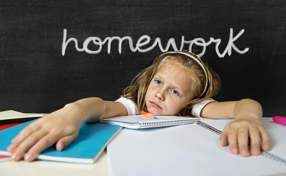 Image is of a child looking distressed while sitting at a desk with schoolwork, concept of an emergency custody attorney addressing concerns affecting a child's wellbeing.