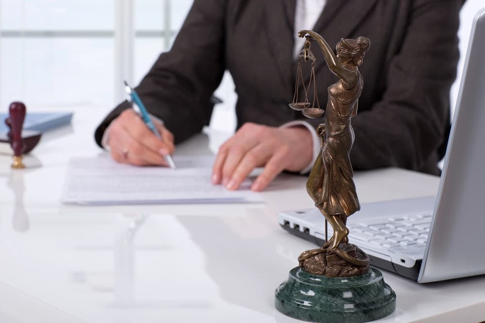 Image is of the Lady Justice statue with an attorney reviewing legal documents, concept of an emergency custody attorney providing legal guidance during an urgent custody matter.