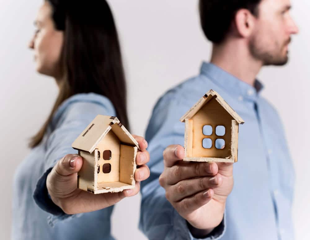 Image is of a separated couple each holding a model house, concept of a property division attorney assisting with the fair division of marital property during divorce.