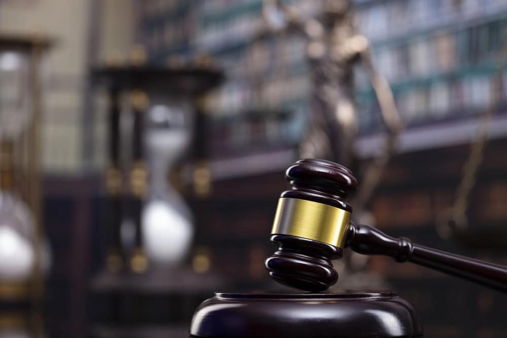 Image is of a judge's gavel in a courtroom with legal symbols in the background, concept of fathers rights attorney.