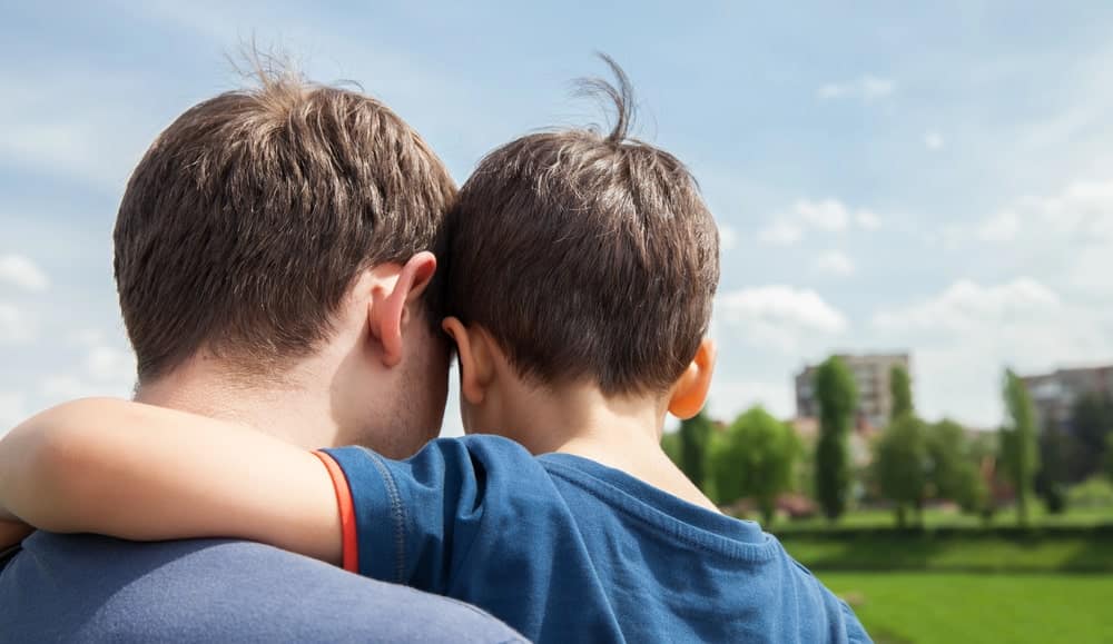 Image is of a father embracing his child in a park, concept of fathers rights attorney.