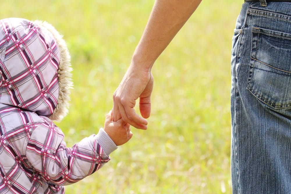Image is of a father holding a young child's hand outdoors, concept of fathers rights attorney.