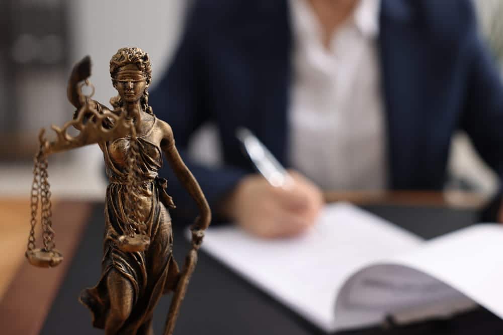 Image is of a lawyer reviewing legal documents with a Lady Justice statue in the background, concept of a grandparents' rights attorney.