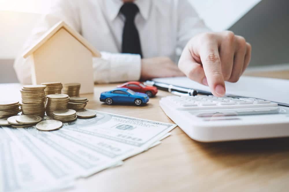 Image is of money, coins, a house model, toy cars, and a calculator on a desk, concept of a legal separation attorney helping clients address property division, debt, and financial matters during separation.