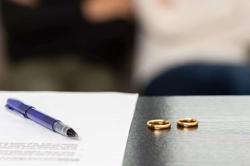 Image is of wedding rings beside a legal document and pen, concept of a legal separation attorney preparing or reviewing a separation agreement.