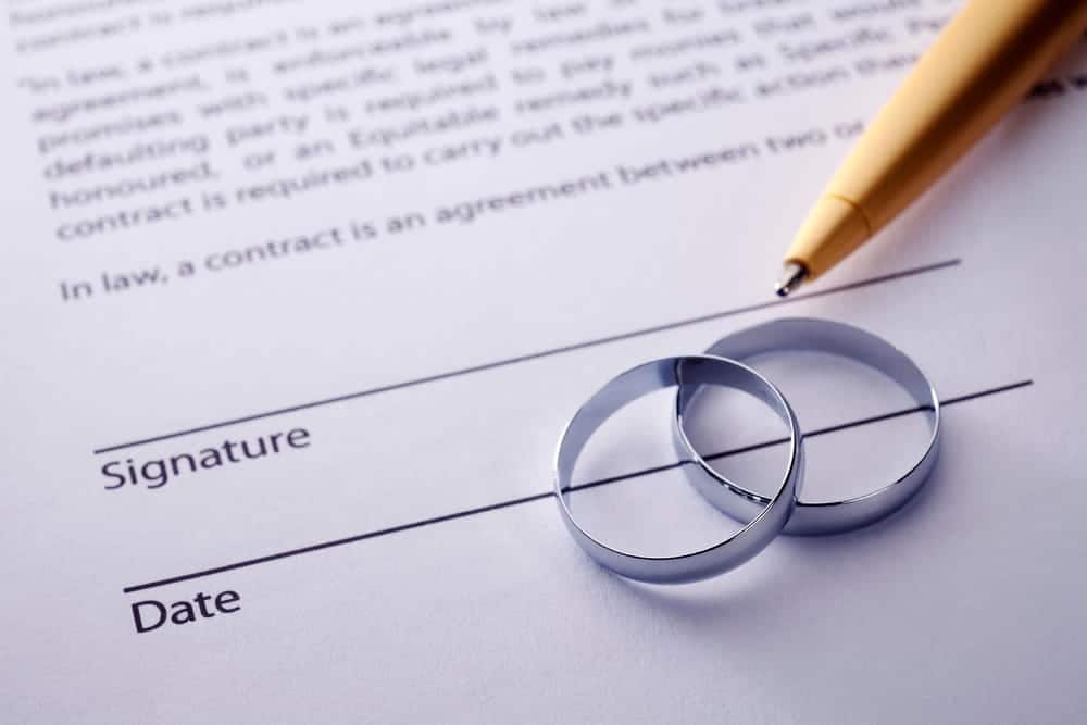 Image is of a signed marital agreement with wedding rings and a pen, concept of postnuptial agreement attorney.
