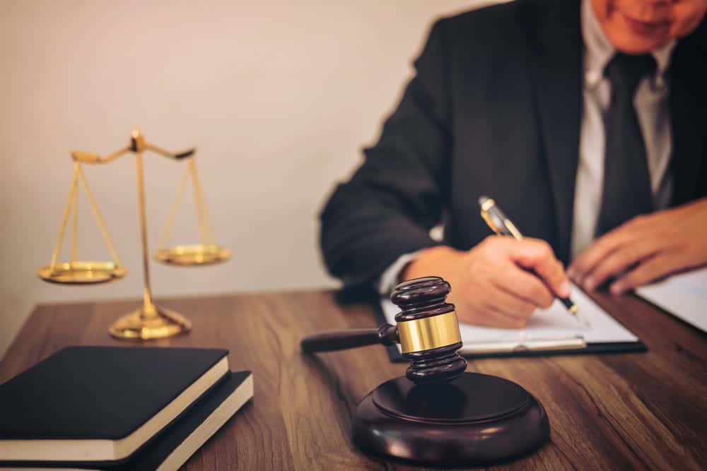 Image is of an attorney drafting legal documents with a judge's gavel and scales of justice nearby, concept of a prenuptial agreement attorney preparing enforceable marital agreements.