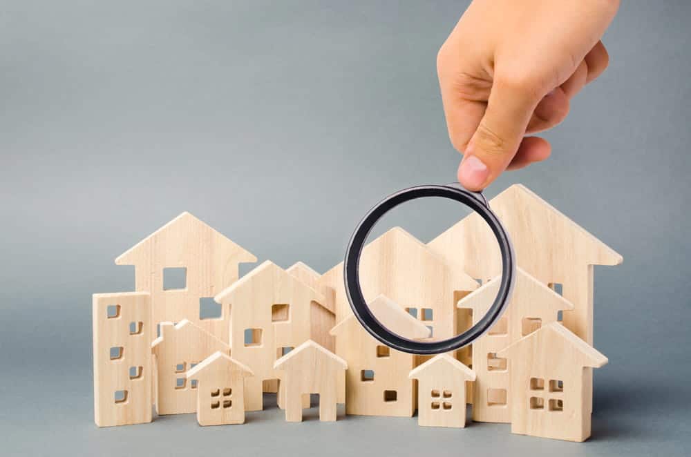Image is of a magnifying glass examining model homes, concept of a prenuptial agreement attorney reviewing property ownership and valuable assets before marriage.