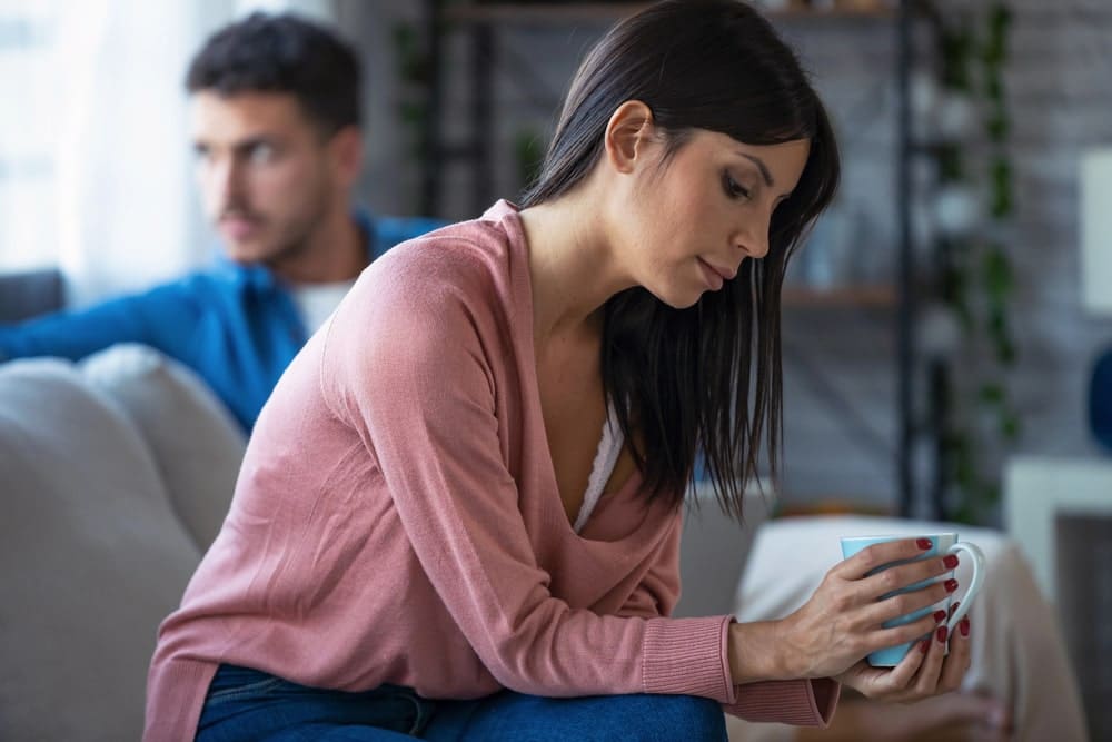 Image is of a spouse sitting alone while the other partner is in the background, concept of a separation agreement helping resolve marital disputes.