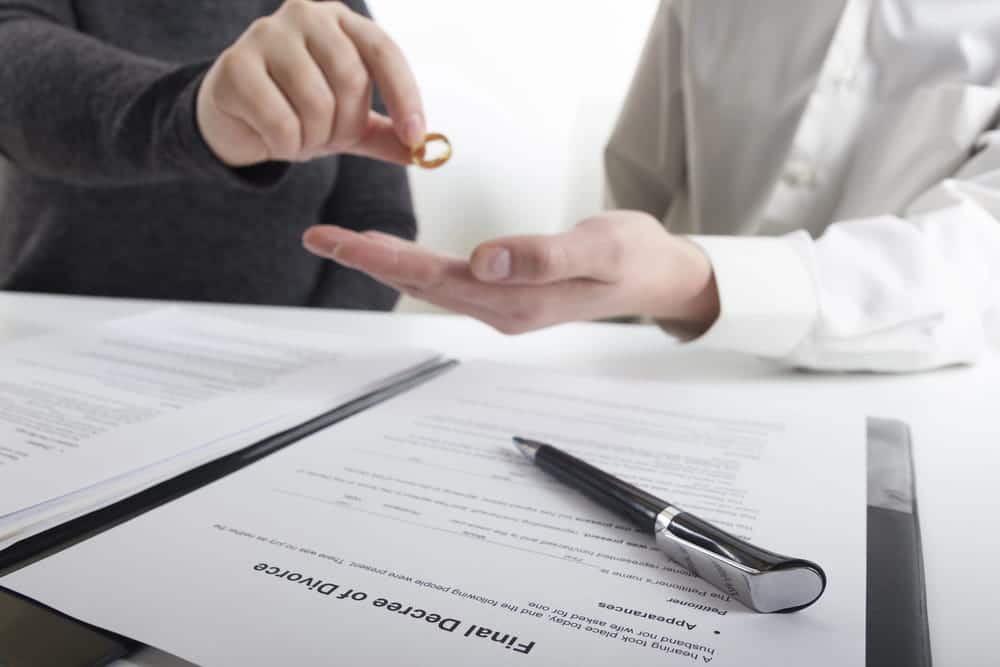 Image is of one person handing a wedding ring to another over divorce documents, concept of uncontested divorce attorney