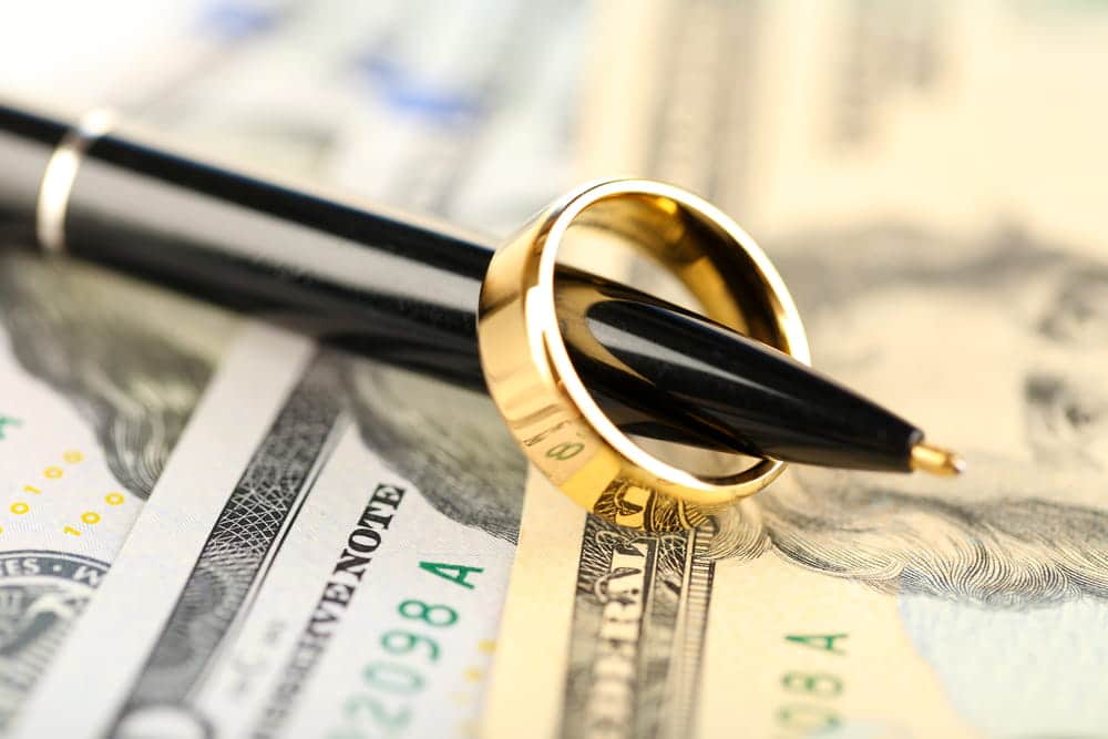 Image is of a wedding ring placed on a pen over currency, concept of uncontested divorce attorney