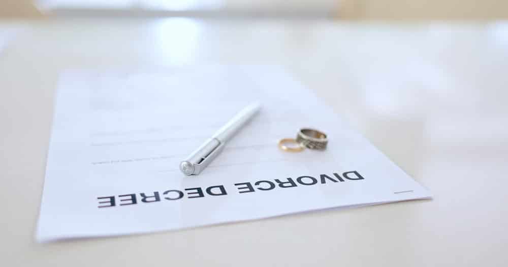 Image is of a divorce decree with wedding rings and a pen, concept of a divorce without lawyer finalizing legal paperwork.