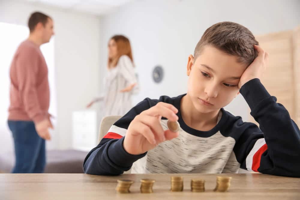 Image is of a child counting coins while parents argue in the background, concept of divorce with children involving child support and financial responsibilities.