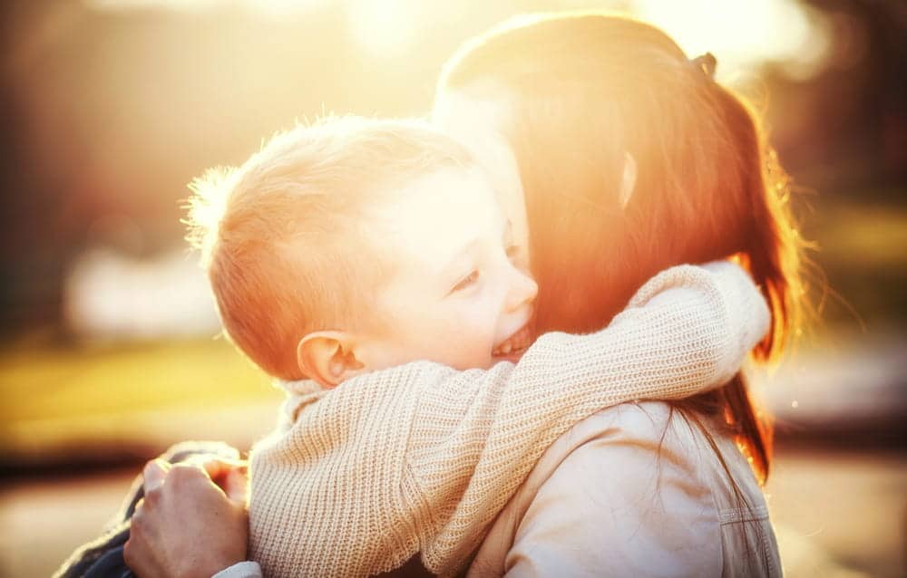 Image is of a young son hugging his mother outdoors, concept of a mothers' rights attorney protecting parental interests