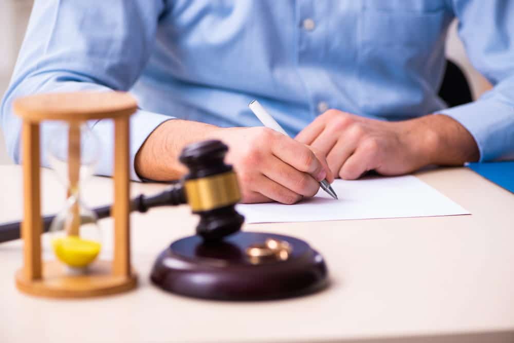 Image is of a person completing legal documents beside a gavel and hourglass, representing the timeline for divorce.