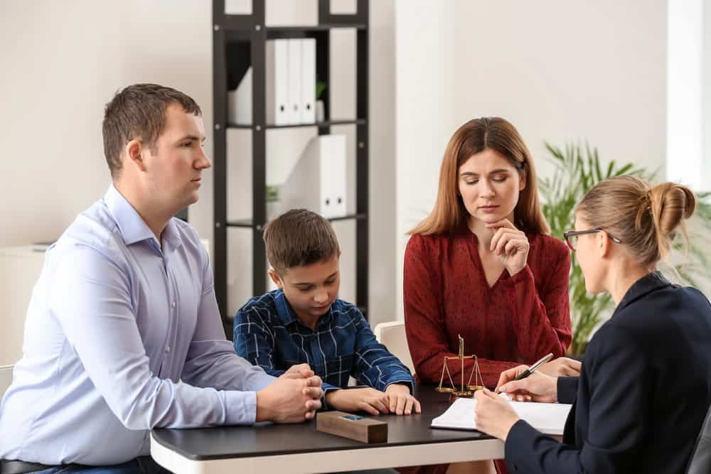 Image is of parents and their child meeting with a legal professional, representing decisions involved in joint custody.