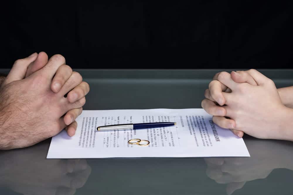 Image is of spouses sitting across from a divorce document and wedding rings, concept of requirements for divorce in North Carolina.