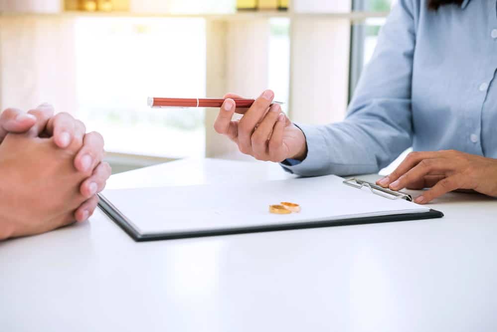 Image is of a legal professional discussing paperwork with a client beside wedding rings, concept of divorce in Charlotte.