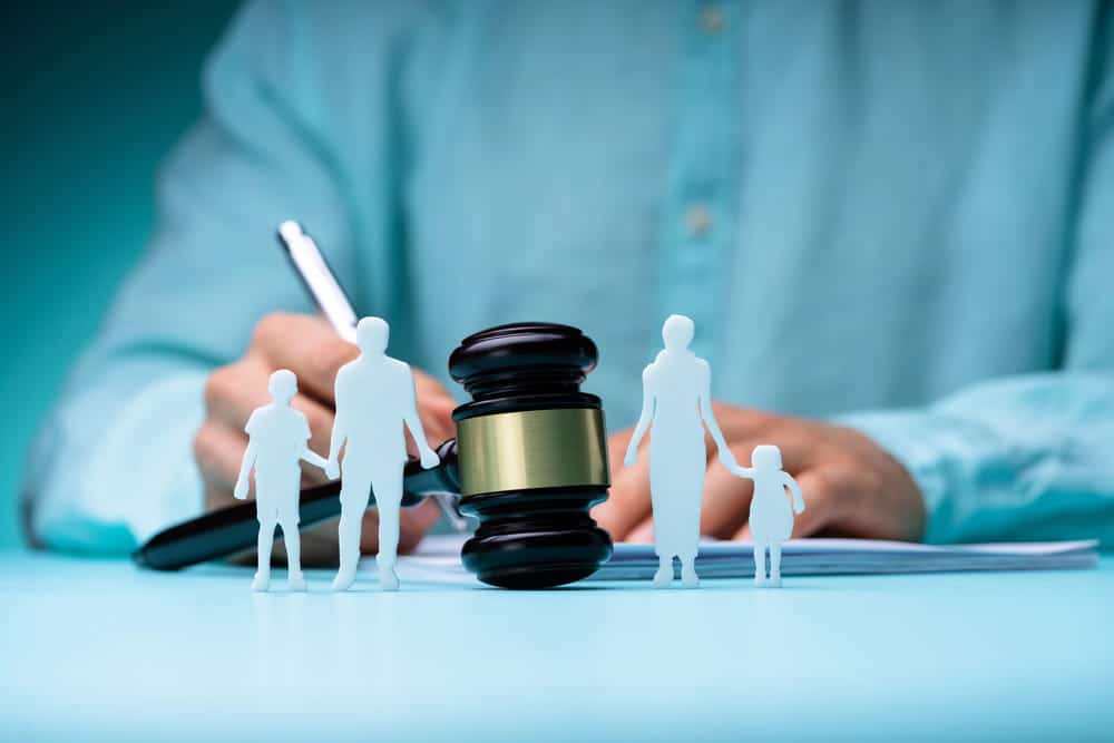 Image is of family figures beside a judge’s gavel, concept of emergency custody proceedings involving parents and children.